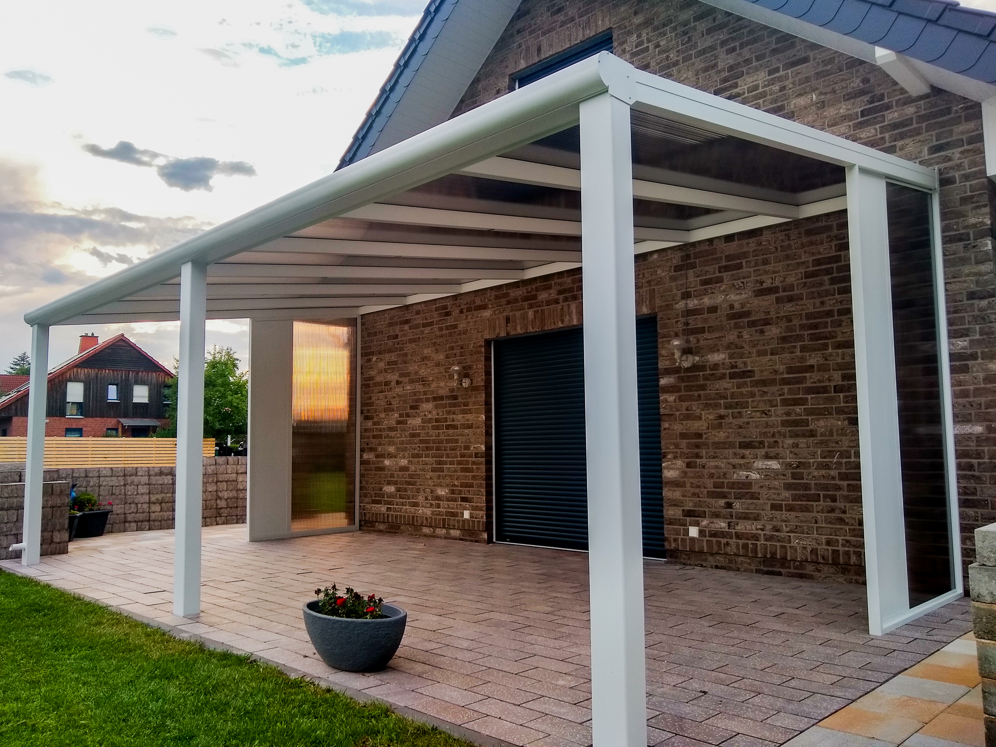 Terrassenüberdachung mit Polycarbonat in Bronze. Alternativ bieten wir auch Glasschiebewand an für Terrasse und Carport aus Aluminium.