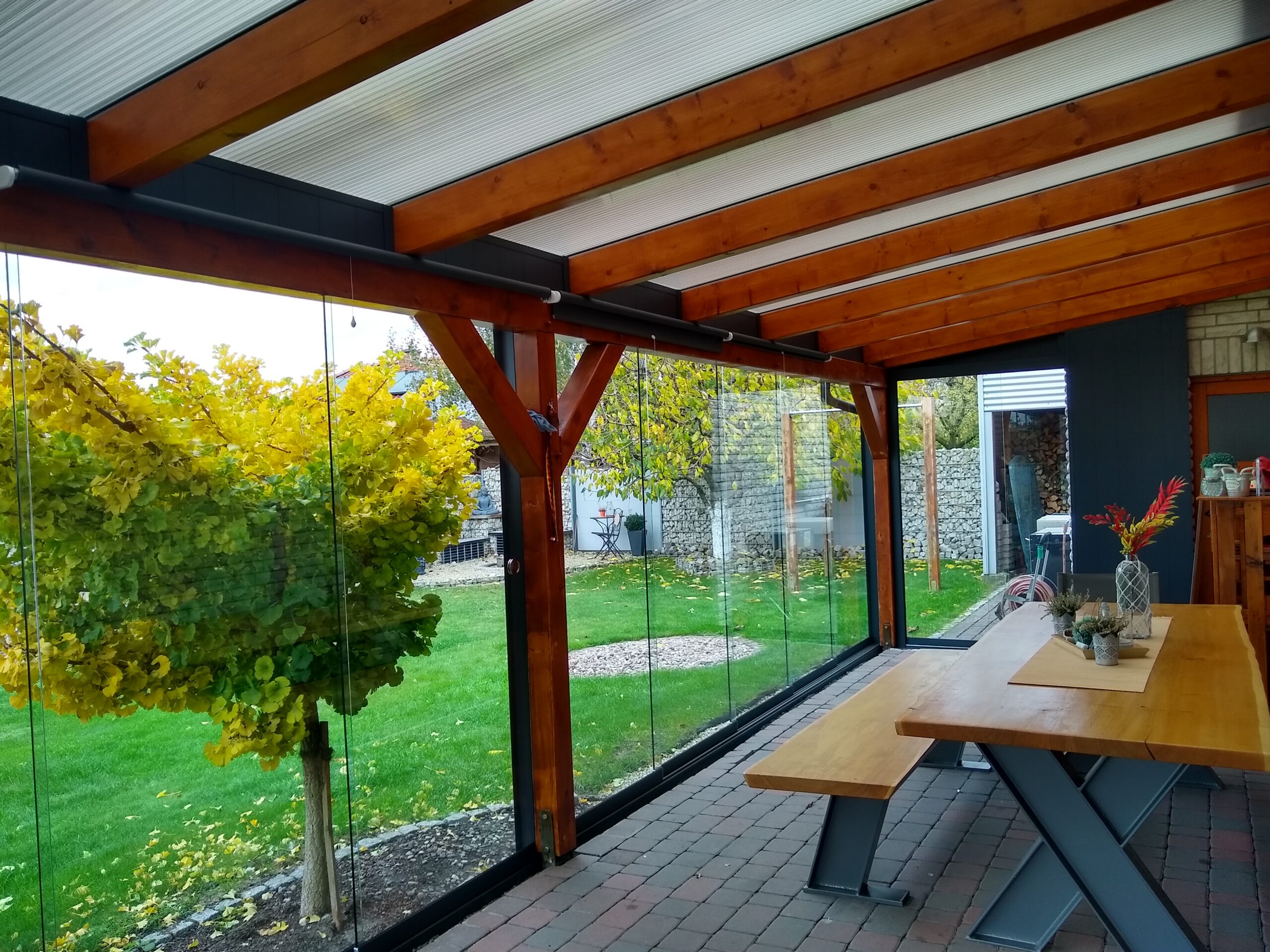 Moderne Holzüberdachung mit integrierter Glasschiebewand für zusätzlichen Schutz und Komfort