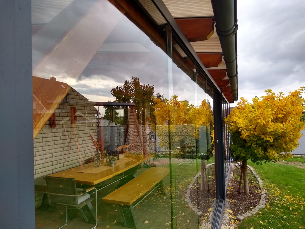 Detailansicht einer modernen Glasschiebewand in einer Holzüberdachung, die flexiblen Schutz und stilvolle Funktionalität bietet