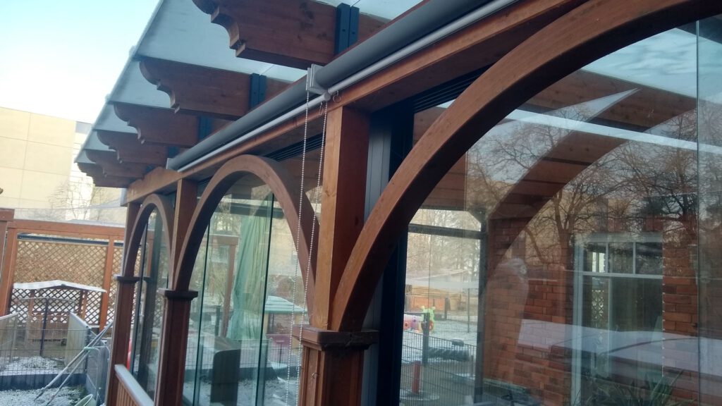 Braune Holzüberdachung mit integrierter Glasschiebewand für optimalen Schutz und stilvolle Flexibilität – perfekt für Garten, Terrasse und Außenbereich.